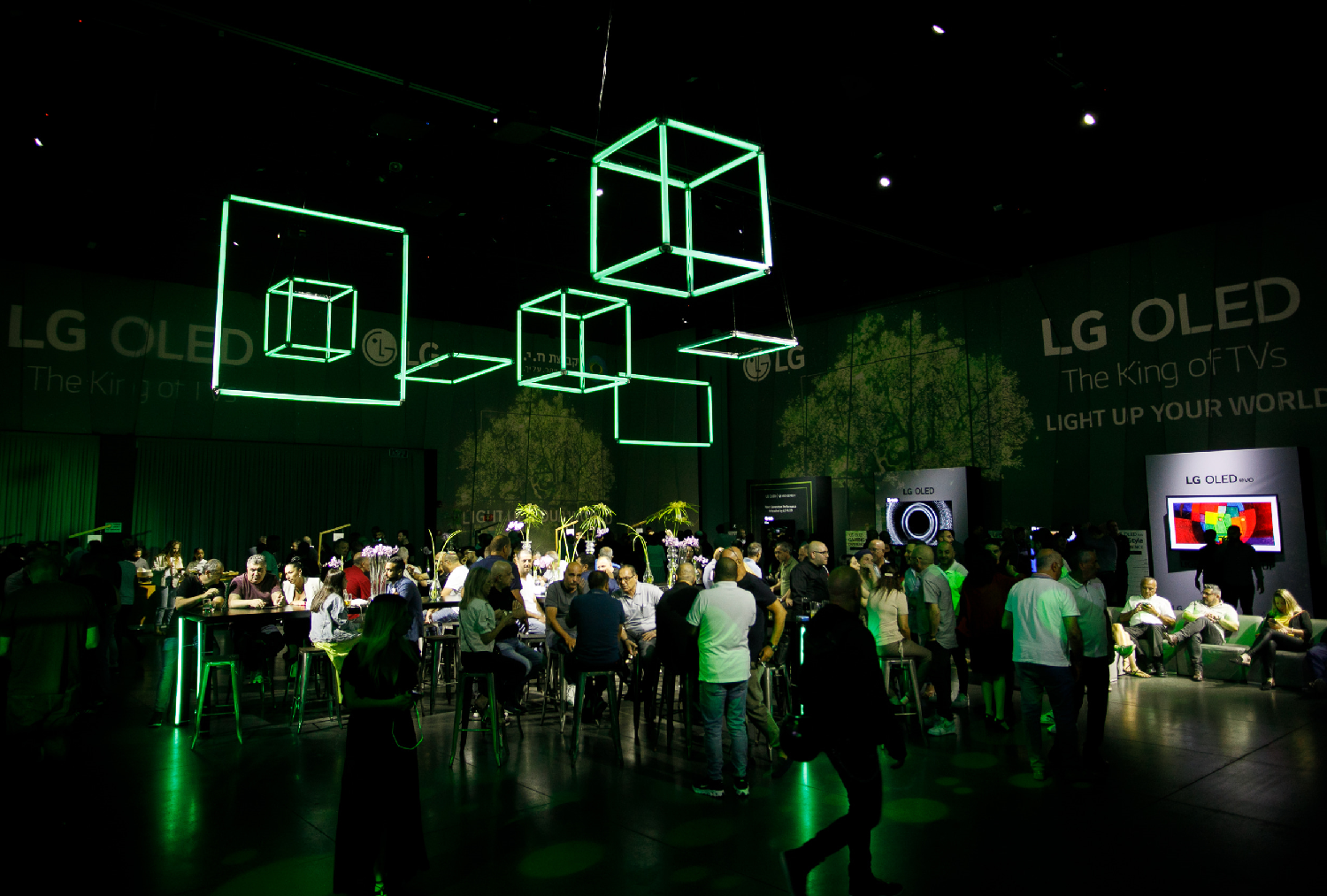 A wide view of the LG 2021 TV launch event in Israel with cubed green neon lighting hanging above a room full of people.