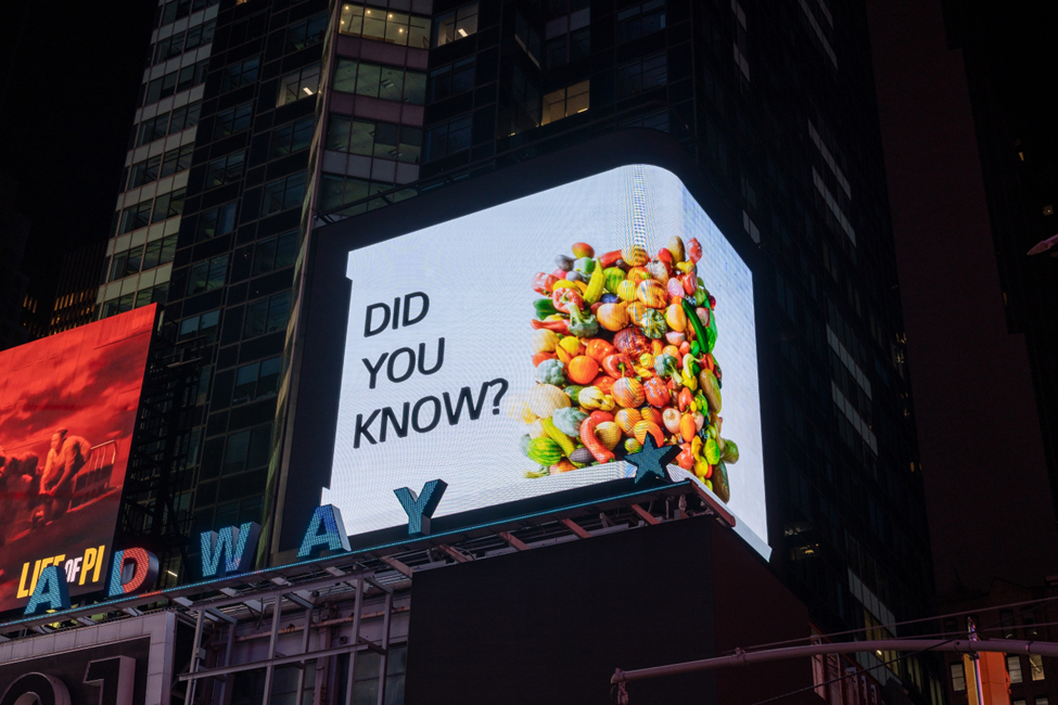 A close-up photo of a billboard in Times Square, New York, displaying a bunch of vegetables with a phrase 