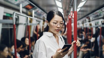 A woman is wearing T90S earbuds while checking her mobile phone on a subway full of people