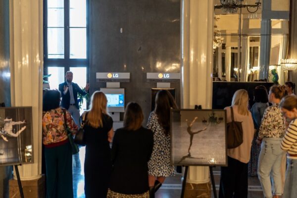 A photo of a man explaining an LG air conditioner on display at the Warsaw Grand Theater, with a back view of people listening to the explanation