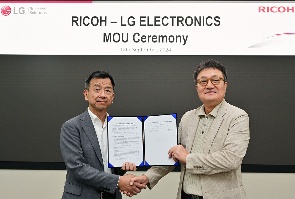 A photo of representatives from LG (left) and Ricoh (right) shake hands while holding a signed MOU