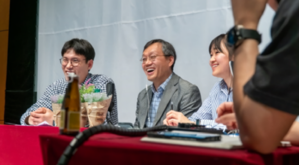 A photo of three people sitting at a red table and smiling