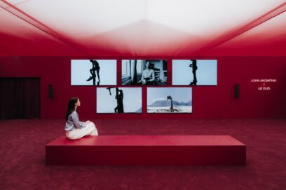 A woman sits on a long bench while looking at artwork presented by John Akomfrah and LG OLED