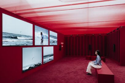 A woman sits on a bench in the middle of the exhibition space, enjoying the artwork of John Akomfrah