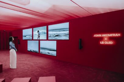 A woman stands in front of five wall-mounted LG OLED TVs, gazing at John Akomfrah’s artwork created in collaboration with LG OLED